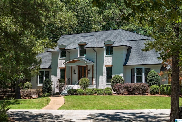 french country style house with a front yard, roof with shingles, brick siding, and mansard roof