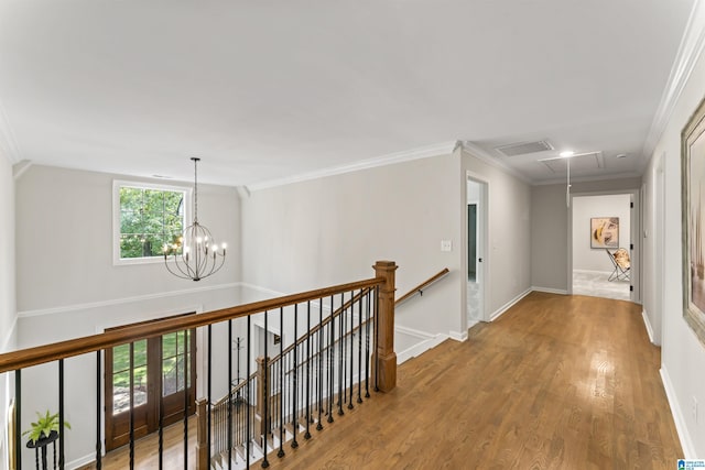 hallway featuring attic access, ornamental molding, wood finished floors, and an upstairs landing