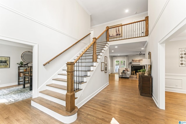 staircase with a fireplace, crown molding, a decorative wall, a towering ceiling, and wood finished floors