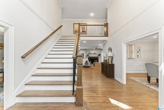 staircase with a fireplace, crown molding, recessed lighting, a decorative wall, and wood finished floors