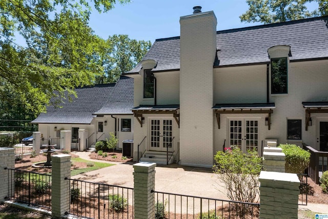 french provincial home featuring french doors, brick siding, a chimney, a shingled roof, and fence