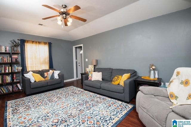 living room with dark wood-type flooring, ceiling fan, and a raised ceiling