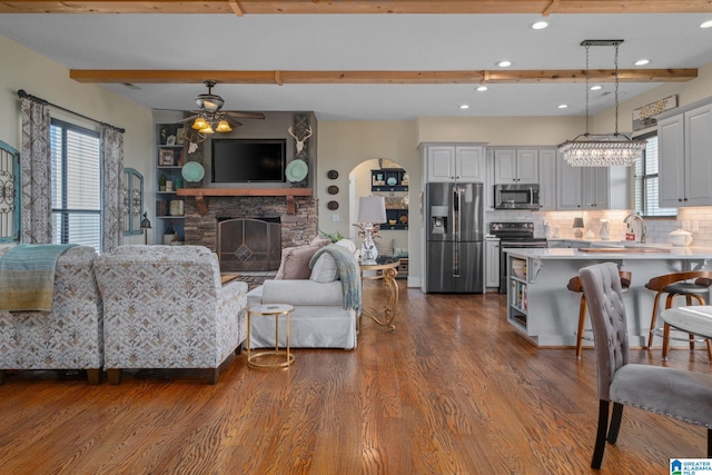 living area featuring arched walkways, dark wood finished floors, ceiling fan, beamed ceiling, and a fireplace