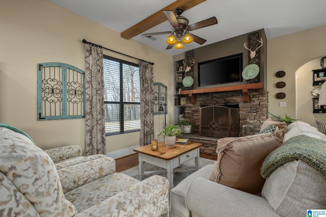 living room featuring ceiling fan, a fireplace, wood finished floors, baseboards, and beamed ceiling