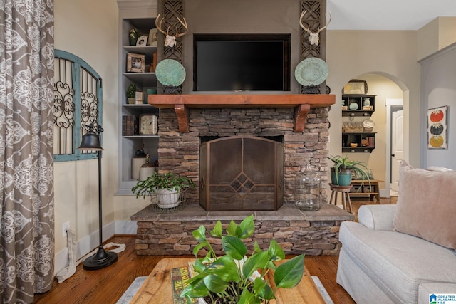 living area with a stone fireplace, wood finished floors, built in shelves, and baseboards