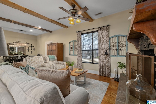 living room with ceiling fan with notable chandelier, a fireplace, wood finished floors, baseboards, and beamed ceiling