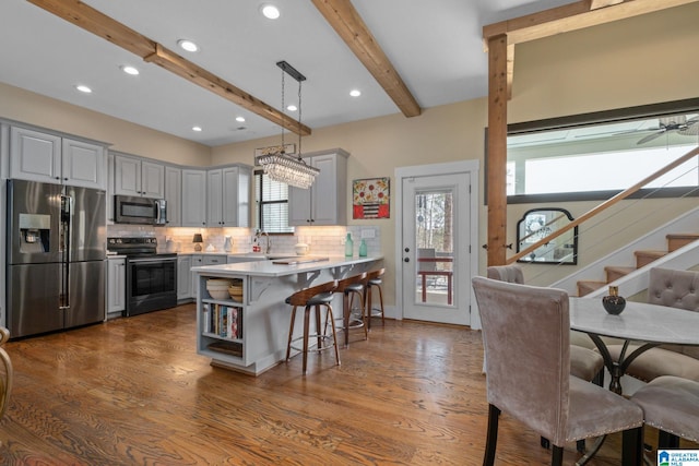 kitchen featuring decorative backsplash, a breakfast bar, stainless steel appliances, gray cabinetry, and beam ceiling