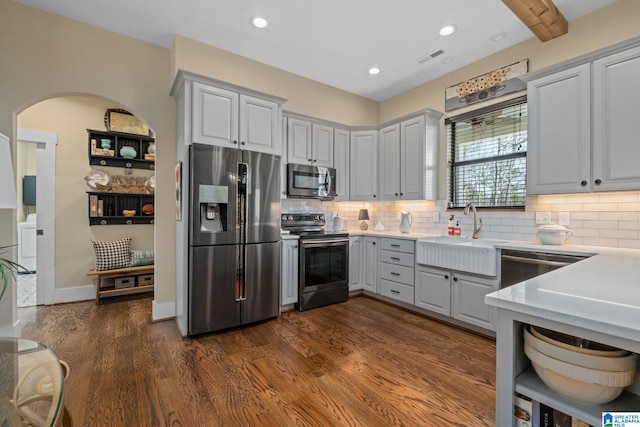 kitchen with appliances with stainless steel finishes, dark wood-style flooring, a sink, and backsplash