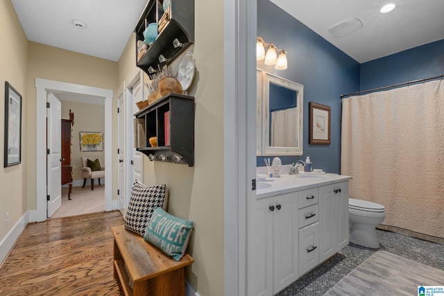 full bathroom featuring double vanity, toilet, a sink, wood finished floors, and baseboards