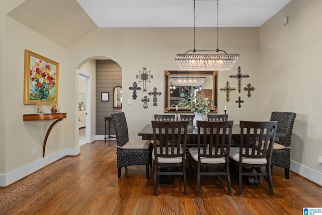 dining area featuring arched walkways, wood finished floors, lofted ceiling, and baseboards