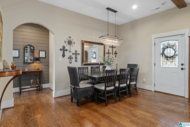 dining space featuring arched walkways, wood finished floors, visible vents, and baseboards