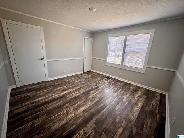 unfurnished bedroom featuring a textured ceiling, baseboards, ornamental molding, a closet, and dark wood-style floors