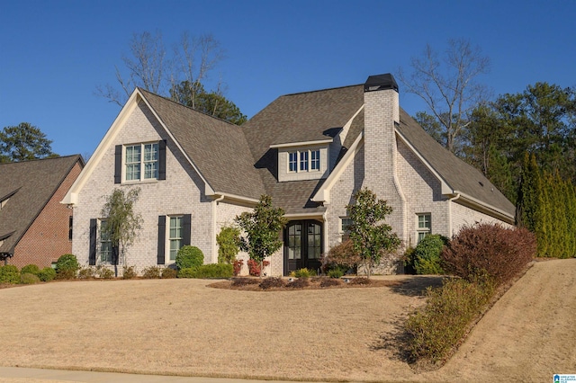 view of front of house featuring french doors, brick siding, a chimney, and a shingled roof