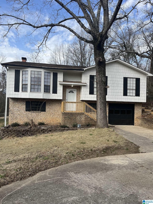 split foyer home featuring a garage, a chimney, concrete driveway, and brick siding