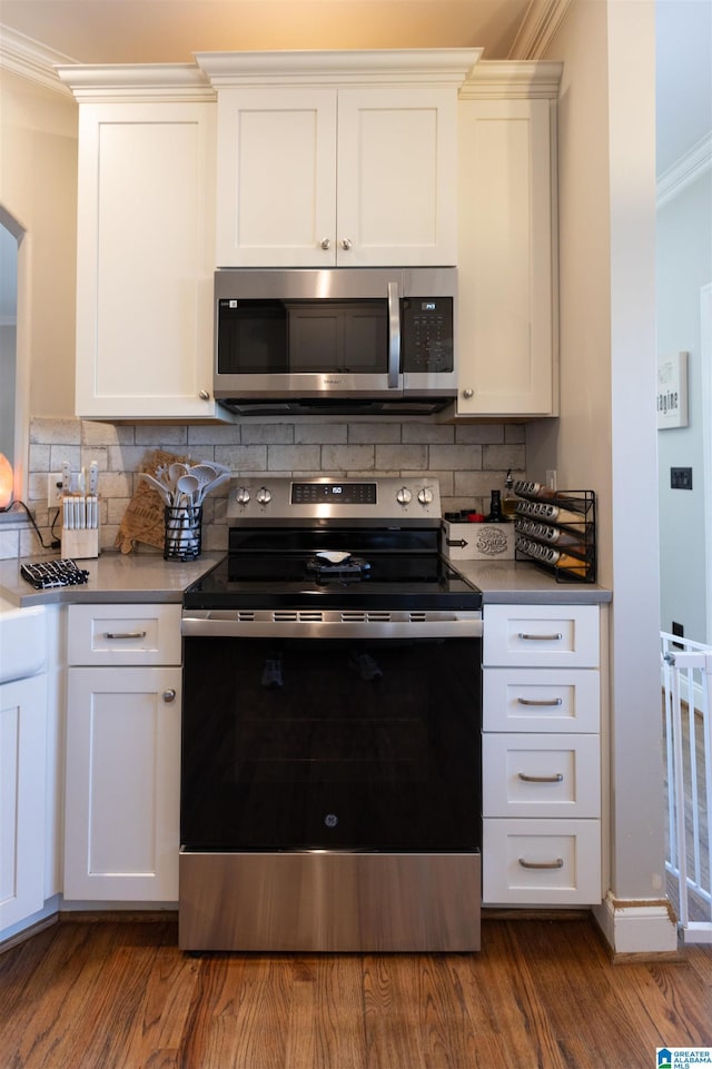 kitchen with crown molding, dark wood finished floors, stainless steel appliances, tasteful backsplash, and white cabinets