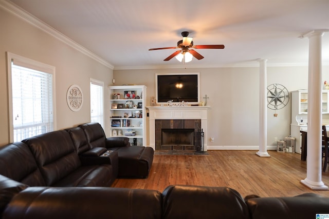 living area with ornamental molding, a fireplace, ornate columns, and wood finished floors