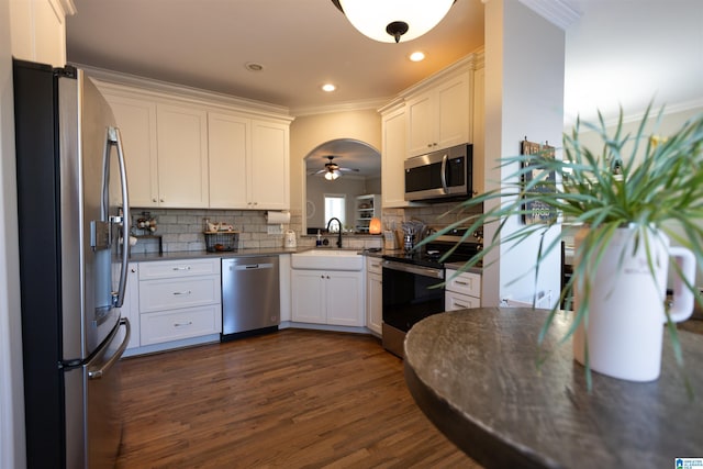 kitchen featuring dark wood finished floors, dark countertops, stainless steel appliances, crown molding, and a sink