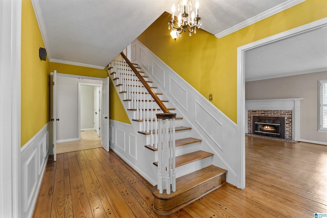 stairs with a fireplace, ornamental molding, hardwood / wood-style floors, and a notable chandelier