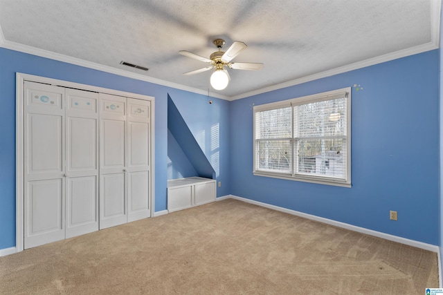 unfurnished bedroom with ornamental molding, a closet, ceiling fan, a textured ceiling, and light carpet