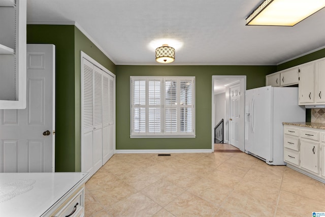 kitchen featuring white refrigerator with ice dispenser, crown molding, and white cabinets