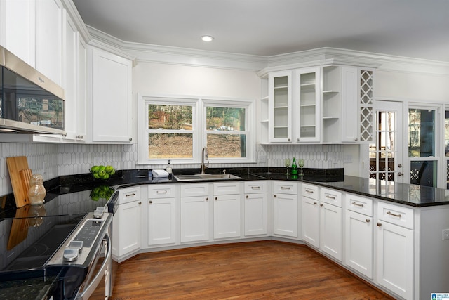 kitchen with white cabinets, ornamental molding, dark stone countertops, stainless steel appliances, and a sink