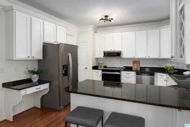 kitchen featuring a breakfast bar, appliances with stainless steel finishes, dark wood-type flooring, white cabinets, and a peninsula