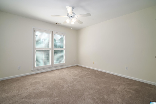 carpeted spare room with visible vents, baseboards, and a ceiling fan