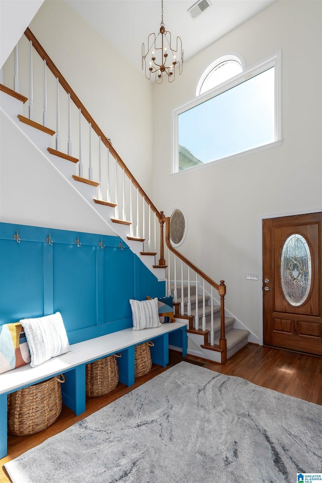 foyer with visible vents, stairway, wood finished floors, a high ceiling, and a chandelier