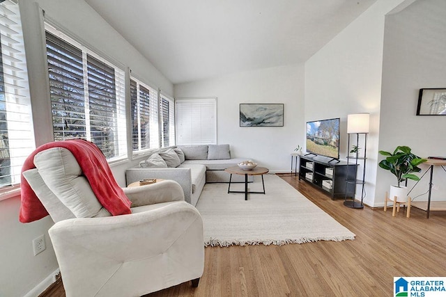 living area with baseboards, vaulted ceiling, and wood finished floors