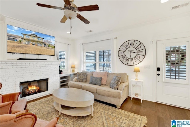 living room with crown molding, visible vents, dark wood finished floors, and a fireplace