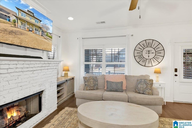 living area featuring dark wood-style floors, crown molding, recessed lighting, visible vents, and a brick fireplace