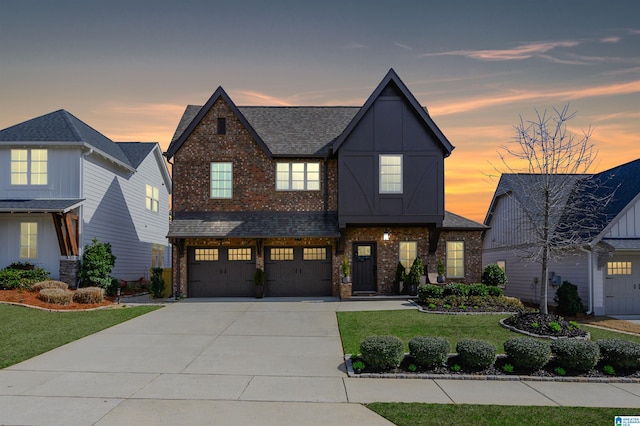 view of front facade with a garage, driveway, a lawn, roof with shingles, and brick siding