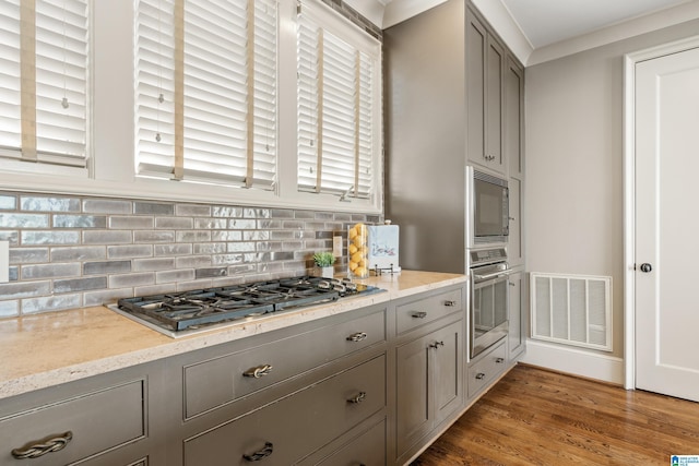 kitchen with gray cabinetry, stainless steel appliances, wood finished floors, visible vents, and backsplash