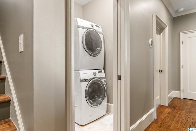 clothes washing area featuring stacked washer / drying machine, laundry area, baseboards, and wood finished floors