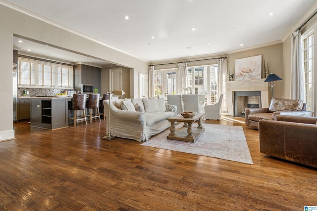 living area with dark wood-style floors, a wealth of natural light, a fireplace, and ornamental molding