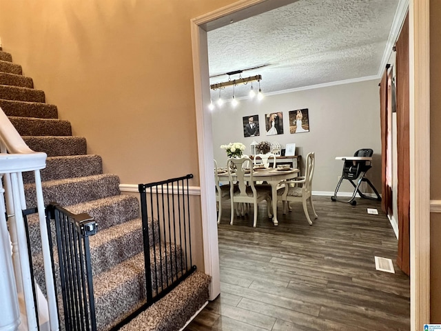 stairway featuring crown molding, visible vents, a textured ceiling, wood finished floors, and baseboards