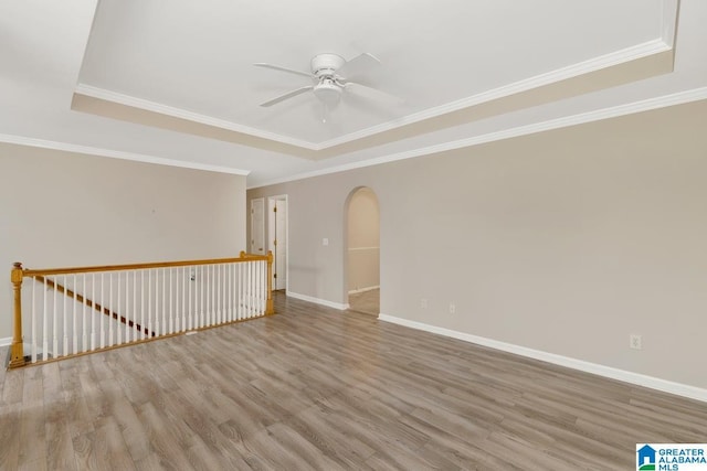 spare room with crown molding, a ceiling fan, baseboards, light wood-style floors, and arched walkways