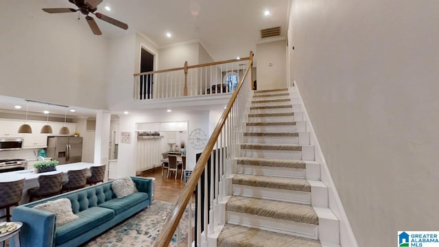 stairway featuring ceiling fan, visible vents, crown molding, a high ceiling, and recessed lighting