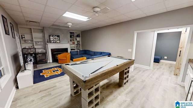 game room with light wood-type flooring, ceiling fan, a fireplace, and a drop ceiling