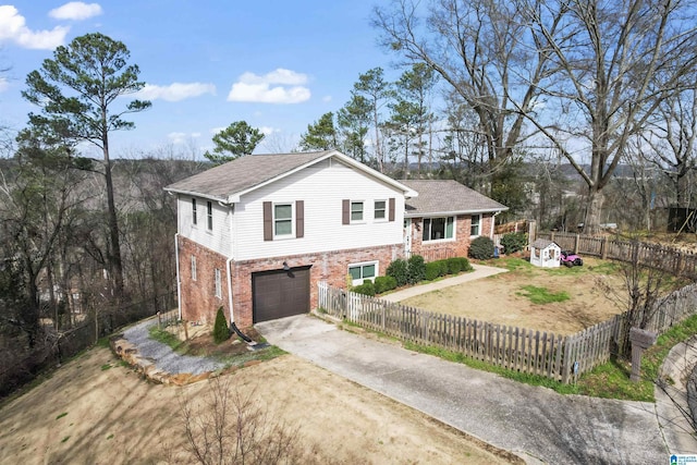 split level home with driveway, brick siding, a fenced front yard, and an attached garage