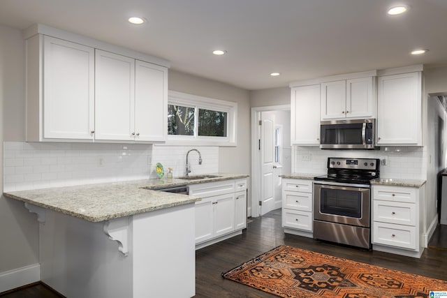 kitchen with a breakfast bar area, appliances with stainless steel finishes, a peninsula, white cabinetry, and a sink