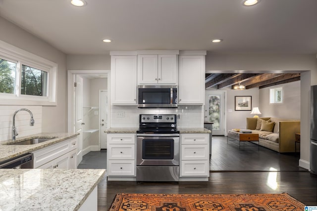 kitchen with stainless steel appliances, light stone counters, a sink, and white cabinetry