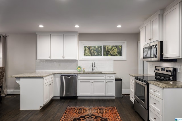 kitchen featuring light stone counters, stainless steel appliances, white cabinets, a sink, and a peninsula