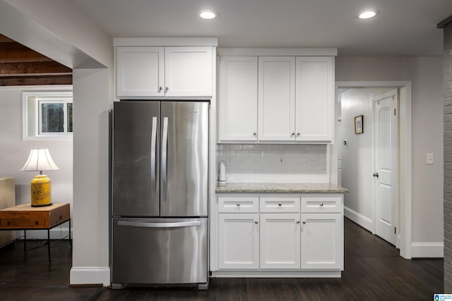 kitchen featuring light stone counters, freestanding refrigerator, and white cabinetry