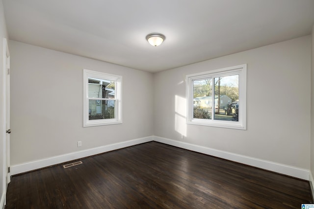 unfurnished room with dark wood-type flooring, visible vents, and baseboards