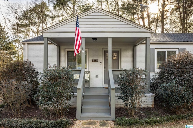 view of front of home with a shingled roof, covered porch, and brick siding