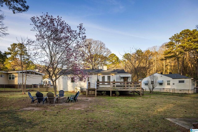 back of property featuring a fire pit, a chimney, fence, a deck, and a yard