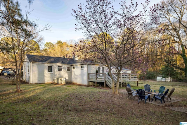 rear view of property featuring an outdoor fire pit, a shingled roof, a lawn, concrete block siding, and a deck