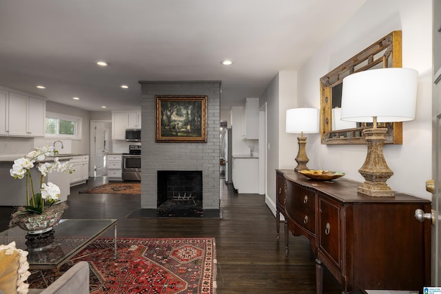 living room with dark wood-style floors, a brick fireplace, and recessed lighting