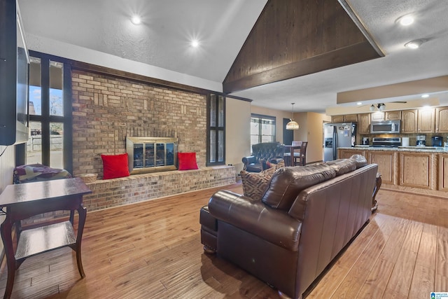 living area with vaulted ceiling, brick wall, a fireplace, and light wood-style flooring